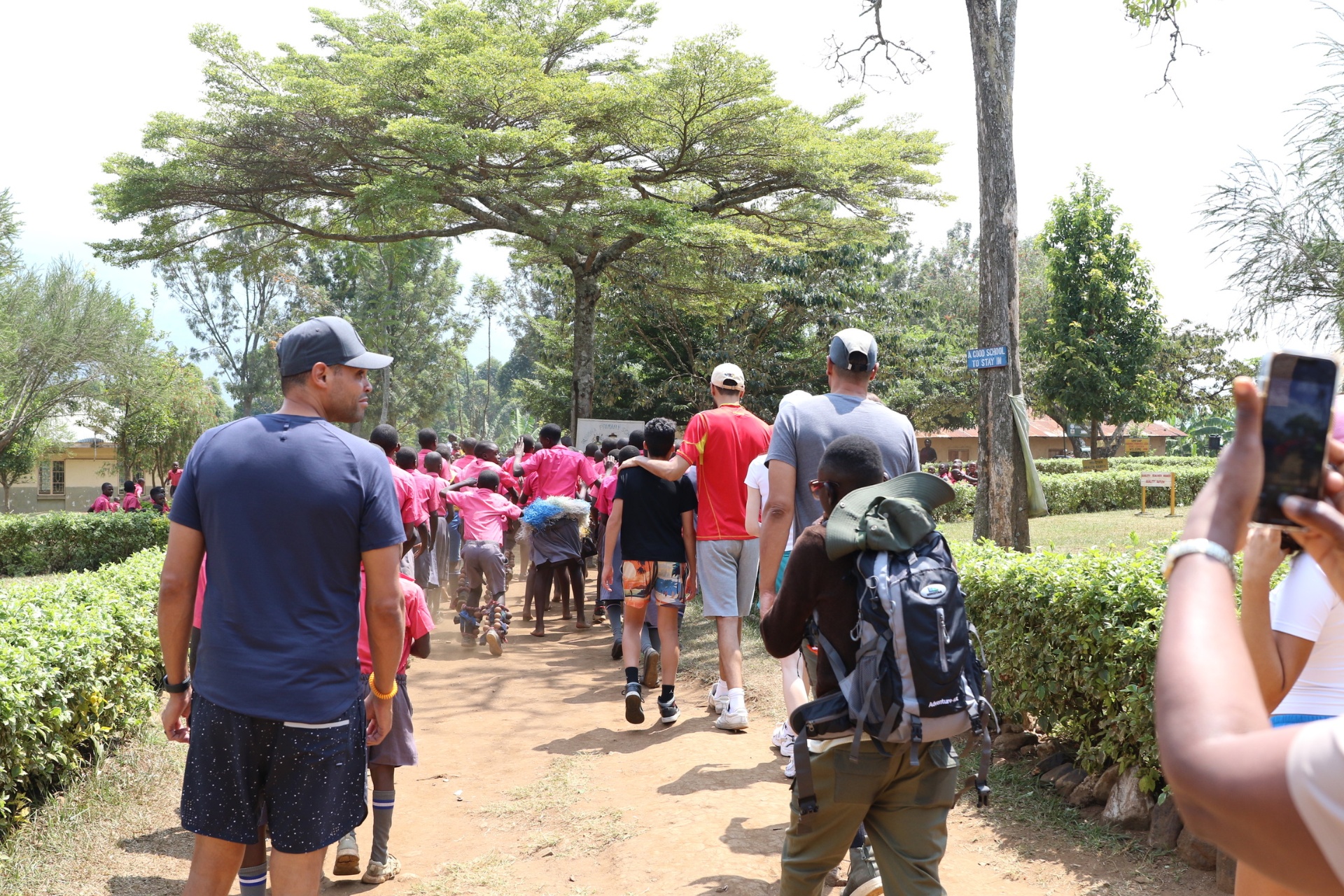 Rubona Primary School grounds with classroom buildings and students gathered on the field.